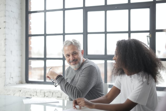 Cheerful senior gray haired mentor supporting young black colleague in office
