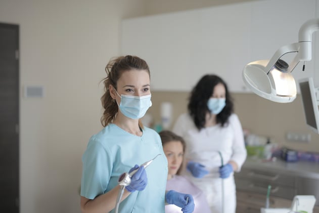 Young female dentist working with assistant while treating patient in modern hospital
